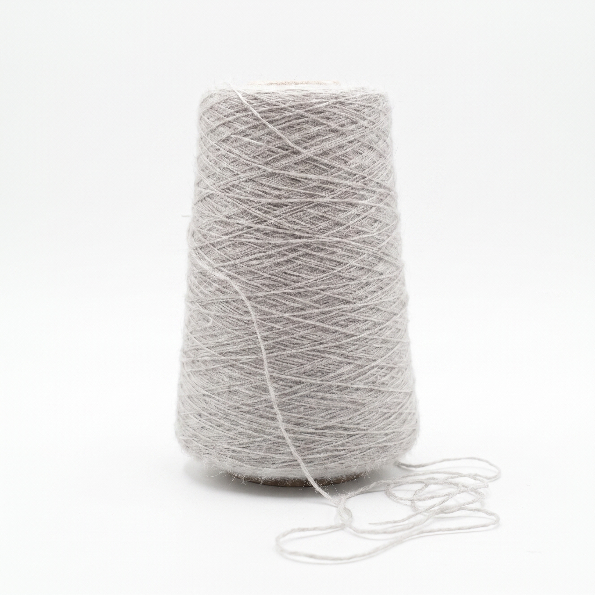 En cone med lysegråt, fiberigt garn og en løs tråd, der ligger foran på en hvid baggrund.